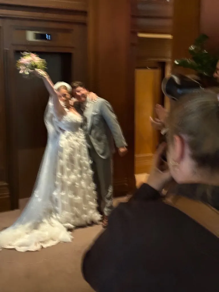 Brautpaar mit hochgehaltenem Brautstrauß wird vor dem Aufzug im Foyer fotografiert