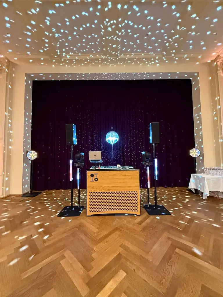DJ-Pult mit Lautsprechern und Discokugel vor der Bühne im Festsaal, Lichtpunkte auf Parkett und Decke