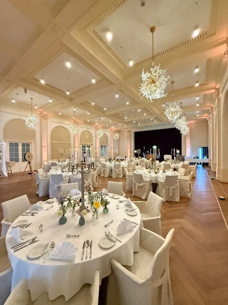 Gedeckte Tische mit Blumenschmuck im Festsaal unter Kronleuchtern und Stuckdecke