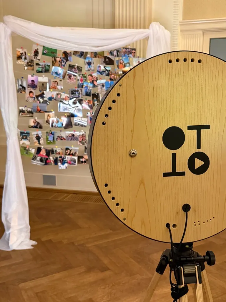 Fotobox mit Holzscheibe und Logo vor einer Fotowand voller Schnappschüsse