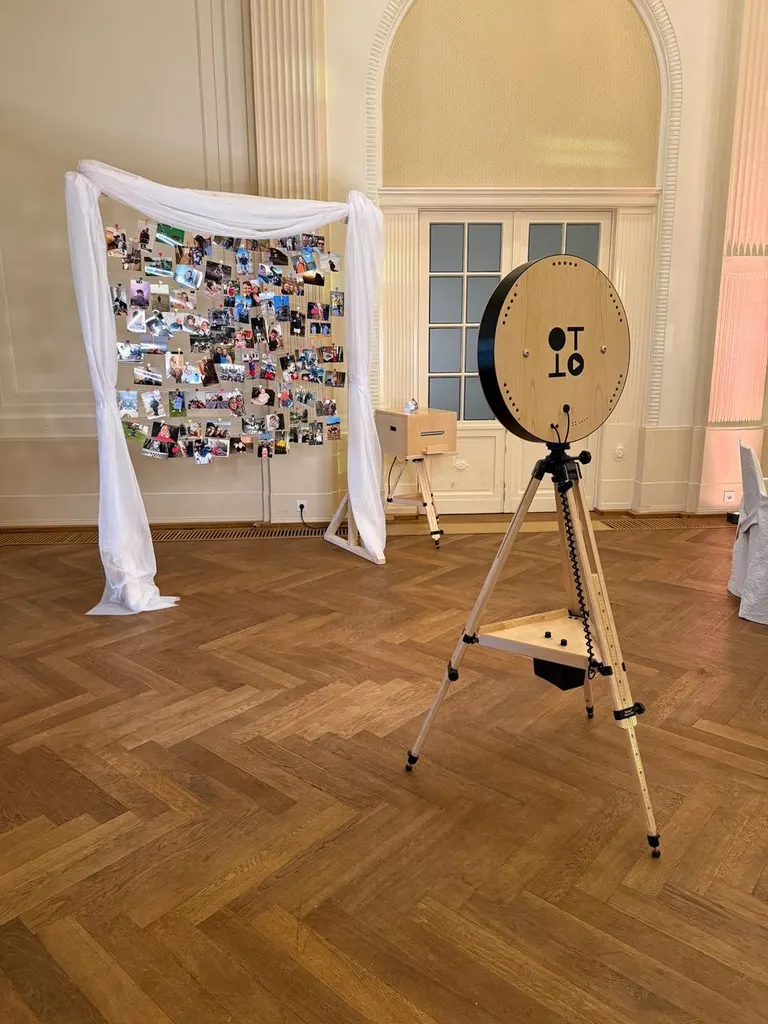 Fotobox auf Stativ neben einer Fotowand mit Stoffbogen vor hohen Fenstertüren