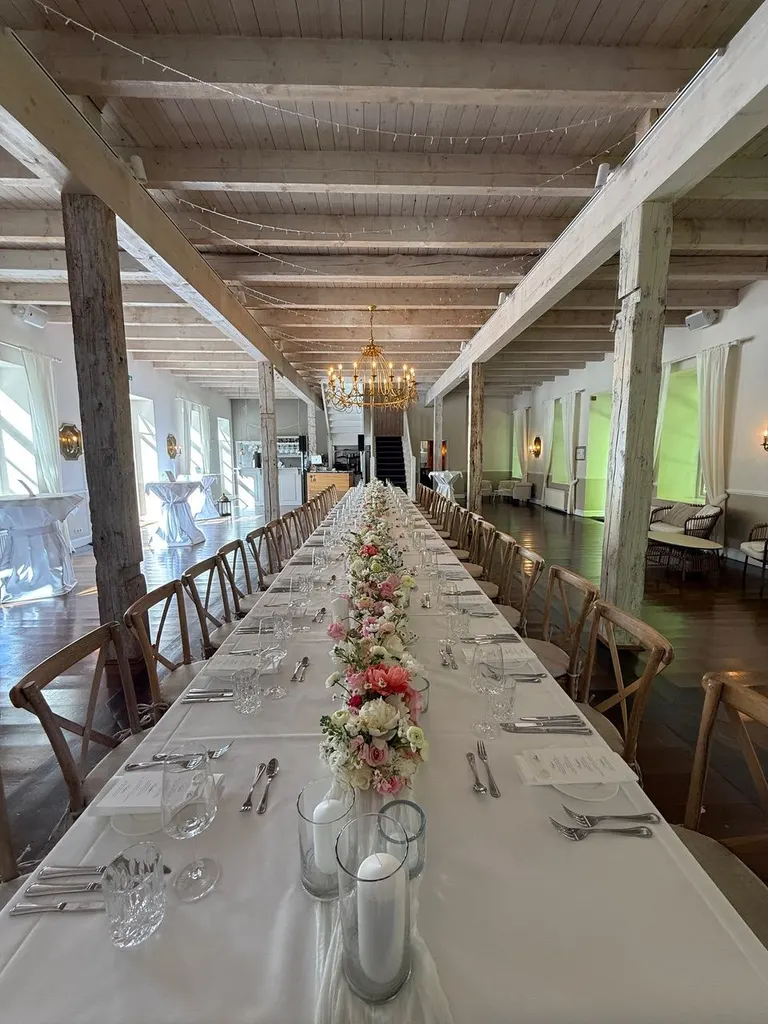 Festlich gedeckte lange Hochzeitstafel mit Blumengesteck im Saal von Gut Pronstorf