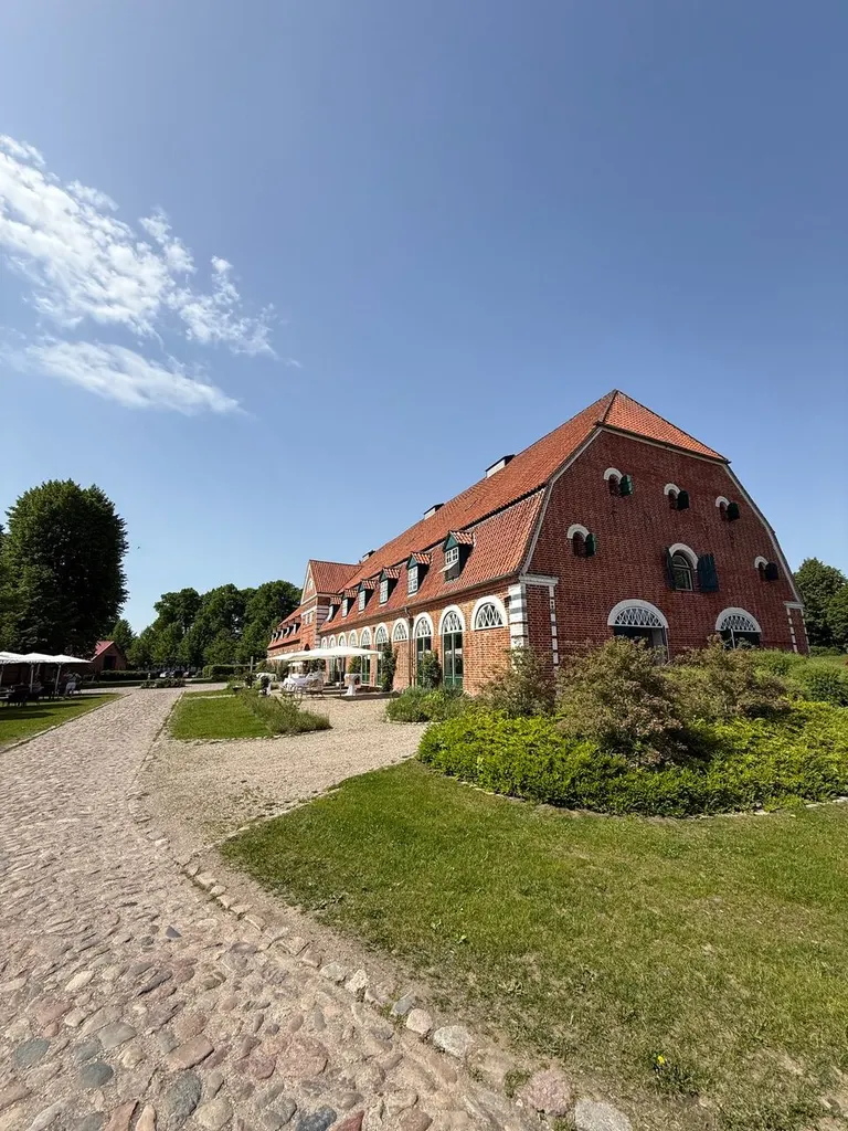 Backsteingebäude von Gut Pronstorf mit Kopfsteinpflasterweg unter blauem Himmel