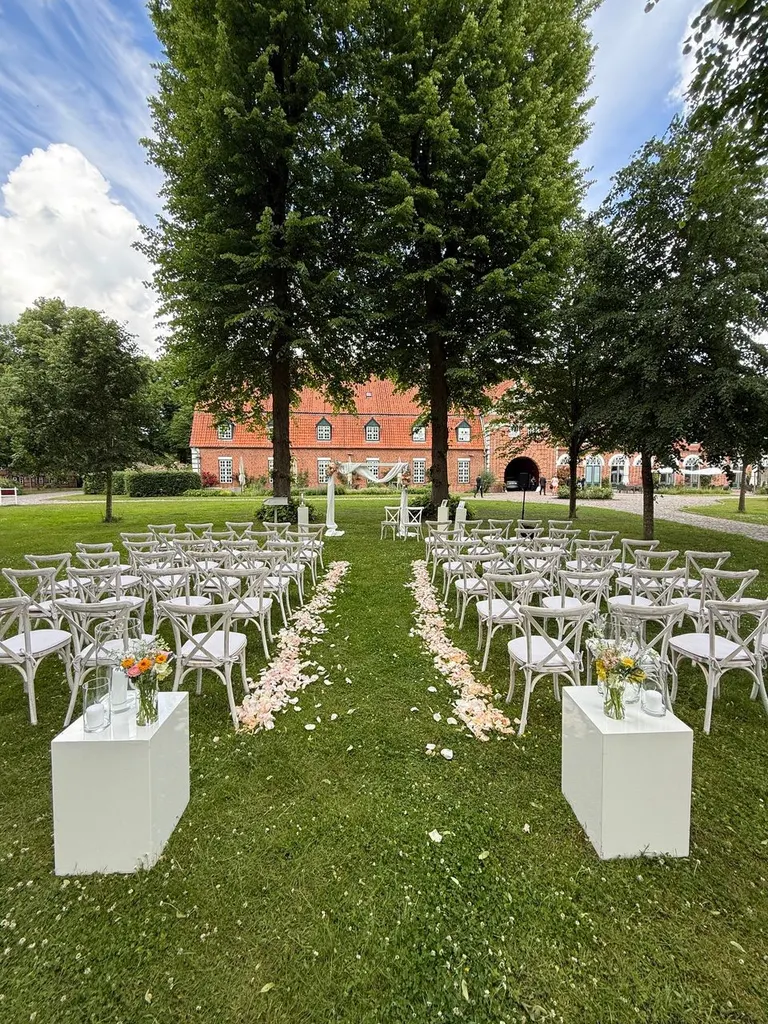Bestuhlung für eine Trauung im Innenhof von Gut Pronstorf mit Rosenblättern im Mittelgang