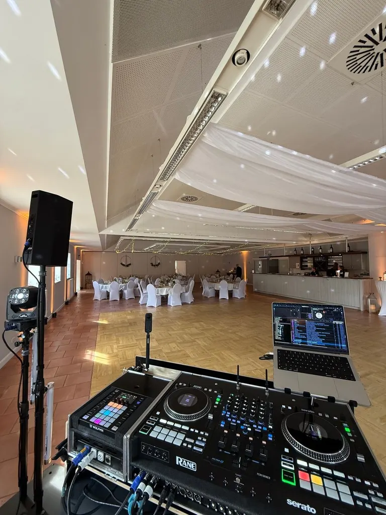 Blick über den DJ-Controller in den langen Festsaal von Gut Steinwehr mit eingedeckten Tischen