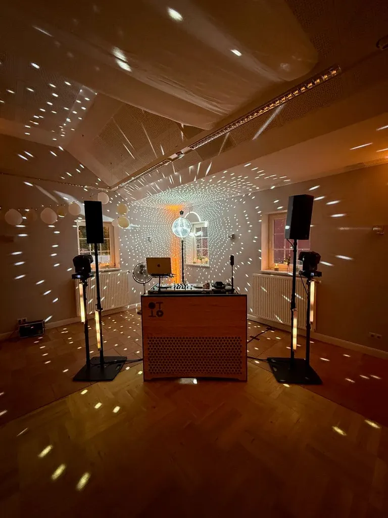 Festsaal von Gut Steinwehr am Abend mit Lichtpunkten einer Discokugel und DJ-Pult