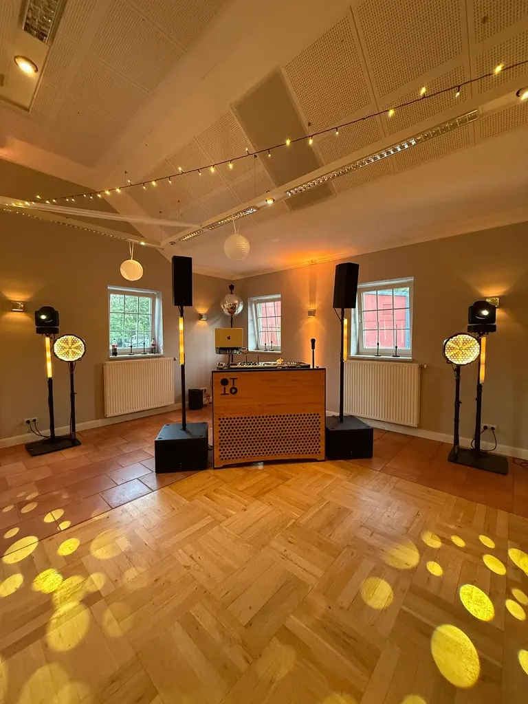 Leerer Festsaal von Gut Steinwehr mit Lichterketten, DJ-Pult und Lautsprechern, goldene Lichtpunkte auf dem Parkett