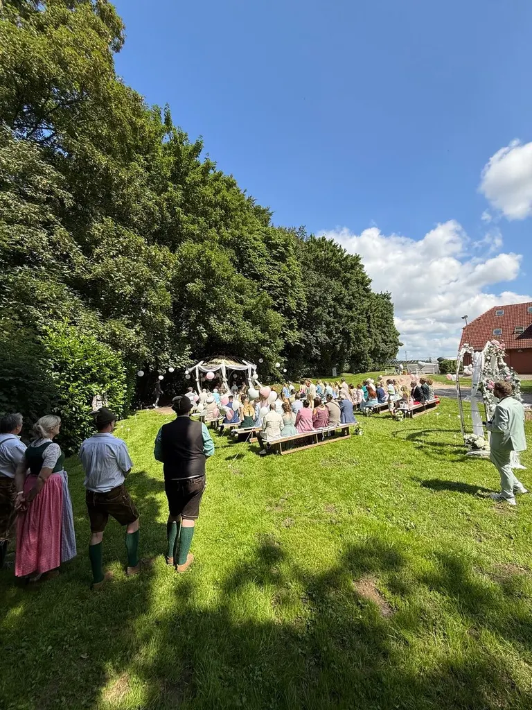 Gäste auf Bänken vor dem Pavillon bei der Trauung auf der Wiese von Gut Steinwehr
