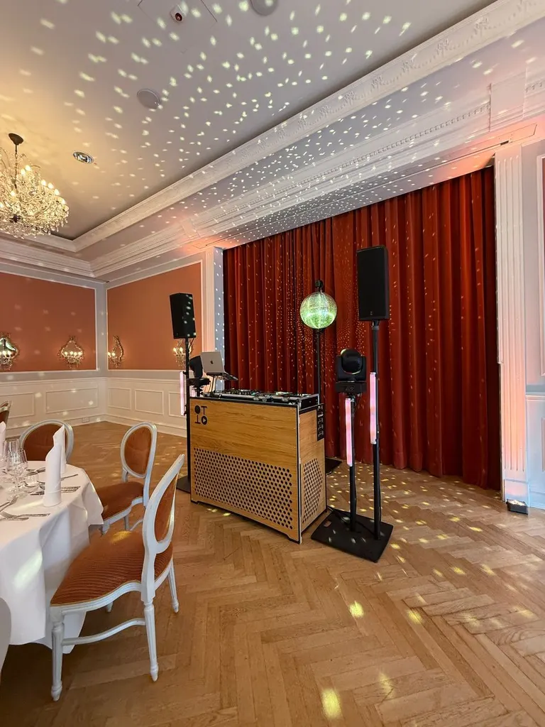 DJ-Pult in Vintage-Holzoptik mit Lautsprechern und Spiegelkugel im Festsaal, rote Vorhänge, Lichtpunkte an der Decke