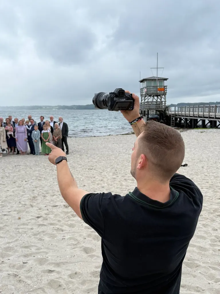Fotograf hebt die Kamera für ein Gruppenfoto der Hochzeitsgesellschaft am Strand
